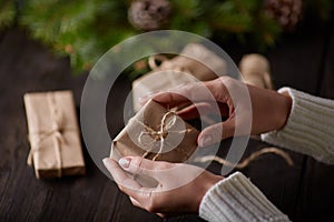Beautiful female hands are packed Christmas gift in brown kraft paper.