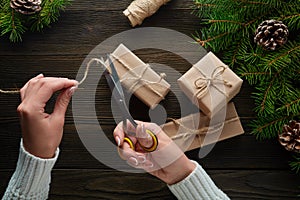 Beautiful female hands with scissors cut off the rope, Christmas gifts in brown kraft paper