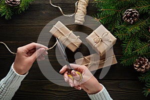 Beautiful female hands with scissors cut off the rope, Christmas gifts in brown kraft paper