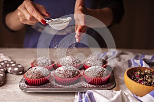 Beautiful female hands sprinkle muffins with powdered sugar.