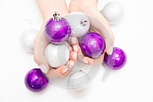 Beautiful female hands with stylish nail manicure polish on winter Christmas balls white background, top view. Skin care