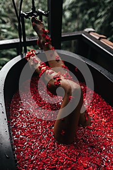 Beautiful female legs in bath with rose petal. Body care.