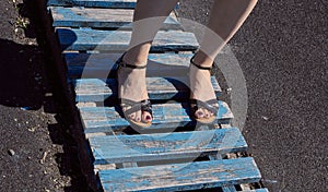 Beautiful female legs in black sandals. Woman's legs wearing sandals. Blue wooden boards.
