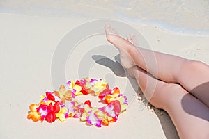 Beautiful female legs on a sandy beach and Hawaiian Lei