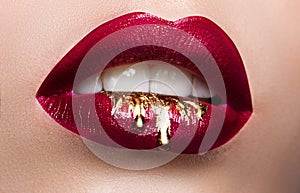 Beautiful female lips closeup. Red lipstick, gold paint flowing over his lips. Stock Photo