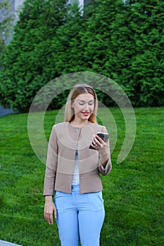 Beautiful female looking at smartphone screen and smiles, stands