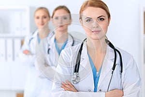 Beautiful female medical doctor standing at hospital in front of medical group. Physician is ready to help patients