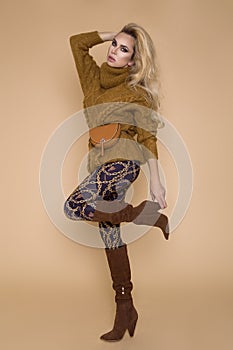 Beautiful female model in a autumn-winter clothing, on a beige background in the studio