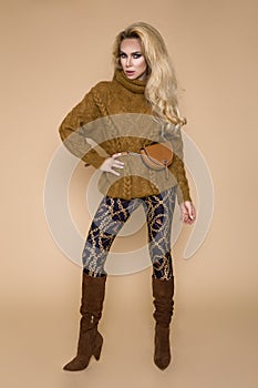 Beautiful female model in a autumn-winter clothing, on a beige background in the studio