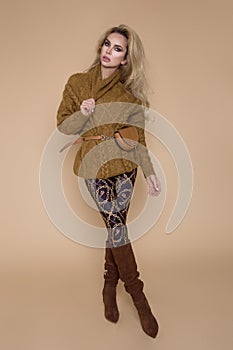 Beautiful female model in a autumn-winter clothing, on a beige background in the studio