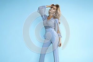 Beautiful female model in a blue elegant jumpsuit posing on a blue background in the studio. High fashion model. Monochrome photo