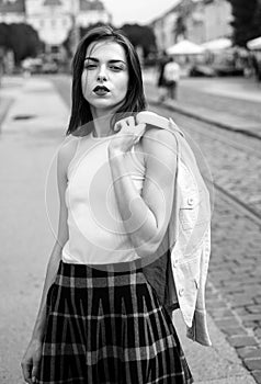 Beautiful female model hold the white suit across sholder in summer city in Europe. Trendy woman posing on the street