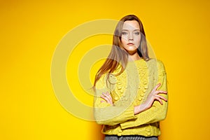 Beautiful female model keeps hands crossed, wears casual comfrotable sweater, poses against yellow background. Copyspace