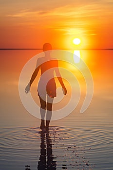 Beautiful female model open arms under sunrise at seaside. Calm water of salt lake Elton reflects woman silhouette. Sun goes