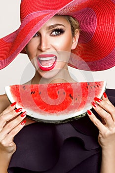 Beautiful female model with perfect face and red hat holding a watermelon at her face