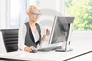 Beautiful female office worker having a break by the computer having a cup of coffee