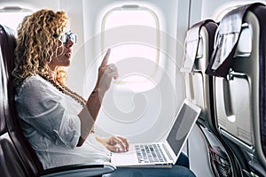 Beautiful female passeger of airplane use personal laptop computer on board with wifi internet connection and ask for hostess help