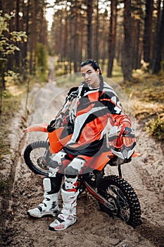 Beautiful female racer sitting on her motocross bike on a trail of sand in the woods