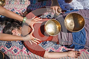 Beautiful female receiving energy sound massage with singing bowls and body massage on a river bank