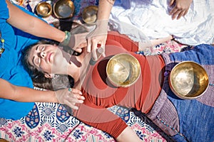 Beautiful female receiving energy sound massage with singing bowls and body massage on a river bank