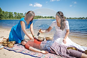 Beautiful female receiving energy sound massage with singing bowls and body massage on a river bank