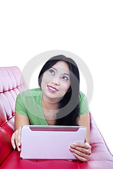 Beautiful female on red sofa using e-tablet, isolated