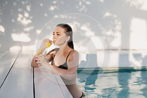 Beautiful female relaxing in summer swim pool and drinking refreshing cocktail.