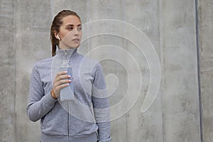 Beautiful female runner is standing outdoors holding water bottle. Fitness woman takes a break after running workout