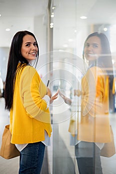 Beautiful female shopaholic looking at fashion boutique showcase holding paper shopping bags