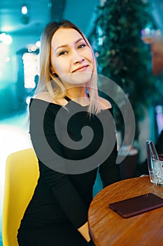 Beautiful female is sitting at table in lounge bar with mobile phone.