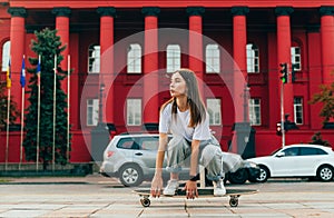 Beautiful female skater in casual clothes at speed rides down the street on a longboard and looks to the side. Woman skater