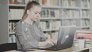 Beautiful female student in headphones sitting at desk in library working concentrated at school project.