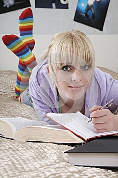 Beautiful Female Student Writing In Book While Lying On Bed