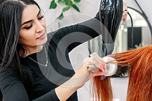 Beautiful female stylist doing hair styling with a hairdryer at a client in a modern beauty salon. Hairdresser doing