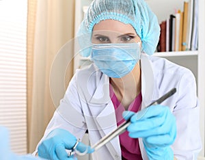 Beautiful female surgeon in mask hold needle, forceps and tweezers