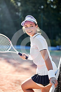 Beautiful female tennis player in white uniform stands next to net posing with racket