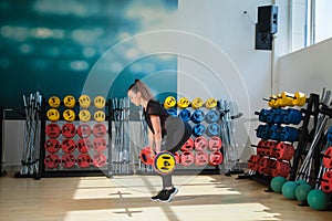 Beautiful female trainer shows exercises with a barbell and dumbbells in the gym