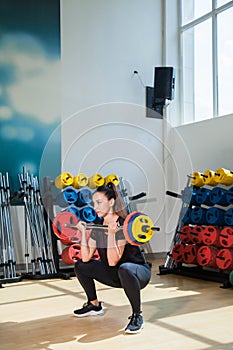 Beautiful female trainer shows exercises with a barbell and dumbbells in the gym