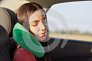 Beautiful female uses neck pillow for sleeping in car, has trip on long distance, trries to relax, feels pain in neck for being in