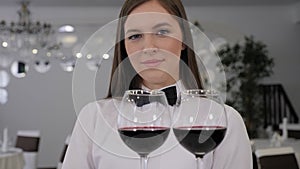 A beautiful female waiter in uniform and white gloves holds a tray of red wine.