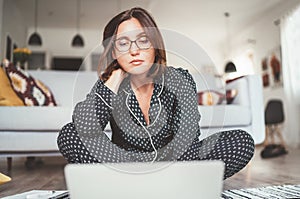 Beautiful female writer dressed pajamas typing notebook keyboard writing novel sitting cross-legged on living room floor with