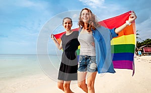 Beautiful female young lesbian couple in love walks along the beach with a rainbow flag, symbol of the LGBT community, equal