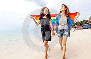 Beautiful female young lesbian couple in love walks along the beach with a rainbow flag, symbol of the LGBT community, equal