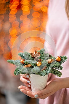 Beautiful festive arrangement of fresh spruce with ball toys in coffee Cup. Christmas mood. Bokeh of Garland lights on