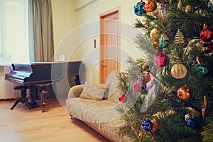 Beautiful festive decorated Christmas tree in living room interior with sofa, piano and window. Concept of new year holiday at co