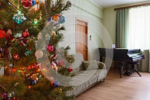 Beautiful festive decorated Christmas tree in living room interior with sofa, piano and window. Concept of new year holiday at co