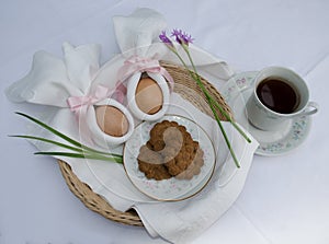 Beautiful festive Easter brunch with eggs in  napkin bunny, cup of tea, cookies and pink flowers on a basket