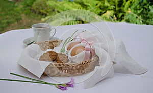 Beautiful festive Easter brunch with eggs in  napkin bunny, cup of tea, cookies and pink flowers on a basket. Easter outdoor