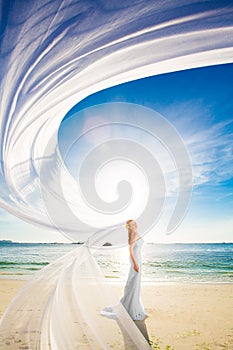 beautiful fiancee in white wedding dress and big long white train, stand on shore sea at sunset