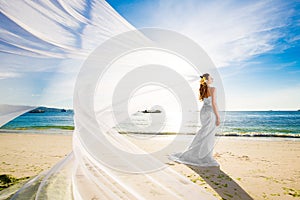 beautiful fiancee in white wedding dress and big long white train, stand on shore sea at sunset